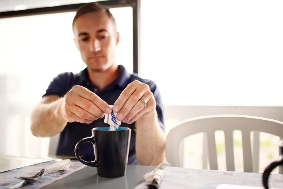 man adding sugar to coffee mug at restaurant table